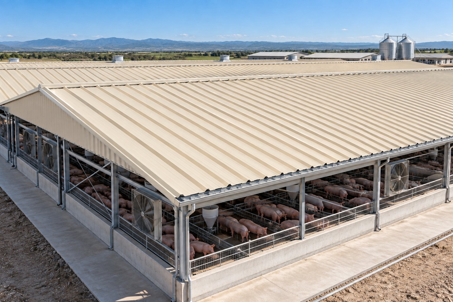 Large livestock feedlot with metal roof structure containing cattle in pens, with mountains visible in the distance