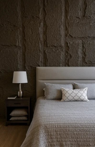 Modern bedroom with gray upholstered bed, decorative pillows, wooden nightstand with table lamp, and textured stone accent wall