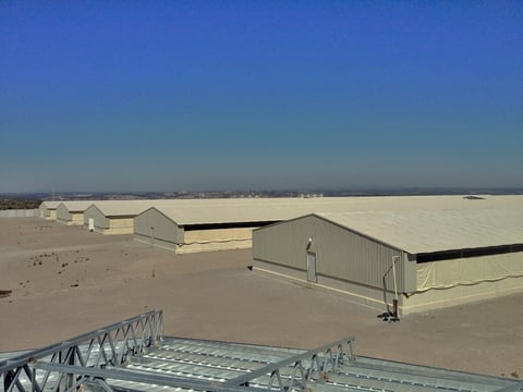 Industrial metal warehouse buildings on desert ground with blue sky and distant cityscape