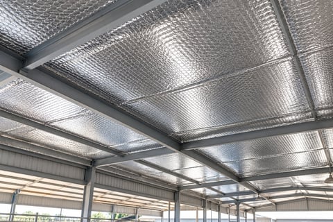 Modern industrial warehouse ceiling with metallic insulation panels and steel support beams letting in natural light