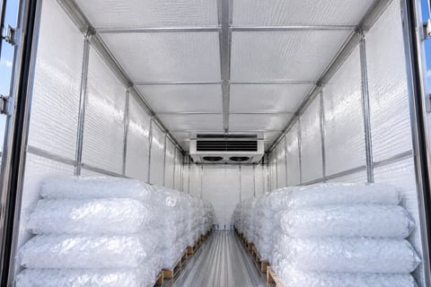 Interior of refrigerated truck loaded with stacked white plastic bags containing frozen goods, with cooling unit visible overhead