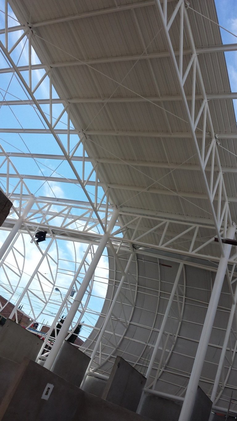 Interior view of modern metal and glass roof structure with white steel framework and exposed trusses against blue sky