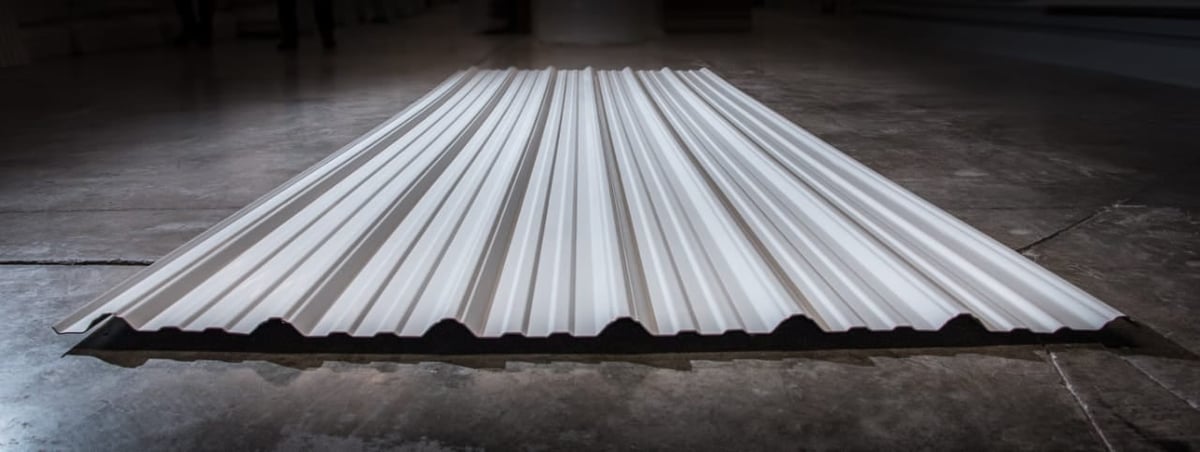 Sheet metal corrugated roofing panel with parallel ridges on concrete floor