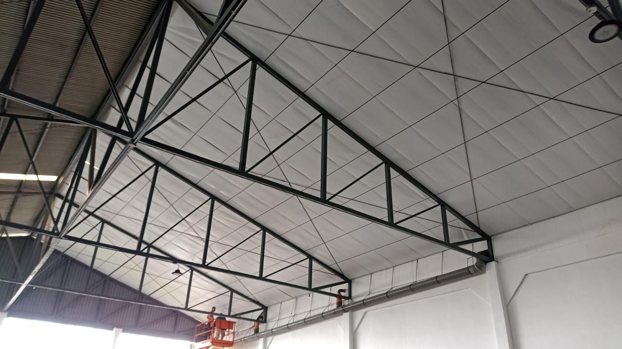 Industrial warehouse interior with metal beam trusses and suspended basketball hoop under drop ceiling